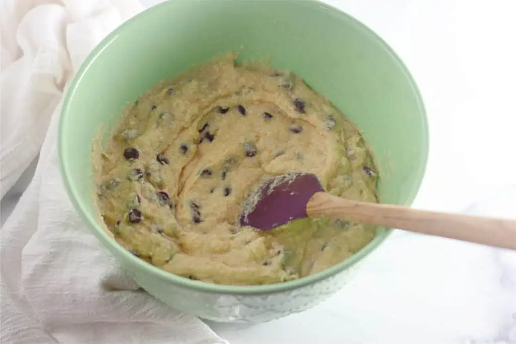 Banana chocolate chip cookie batter in a bowl with a wooden spoon.