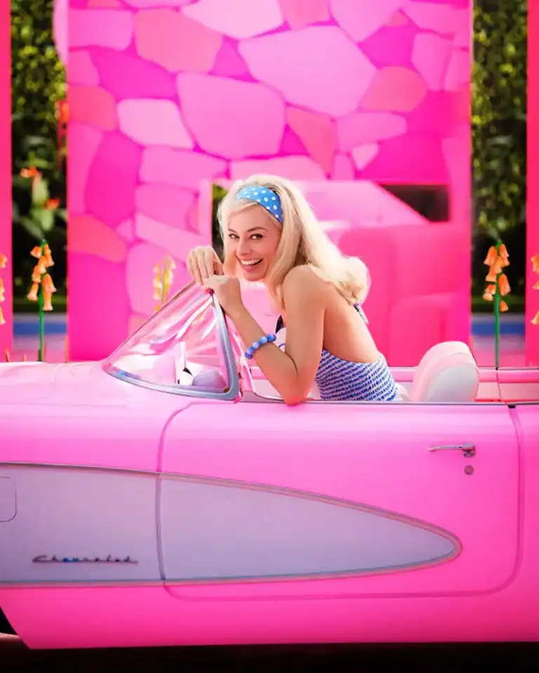 A blonde woman sitting in a pink car receives free Barbie movie tickets.