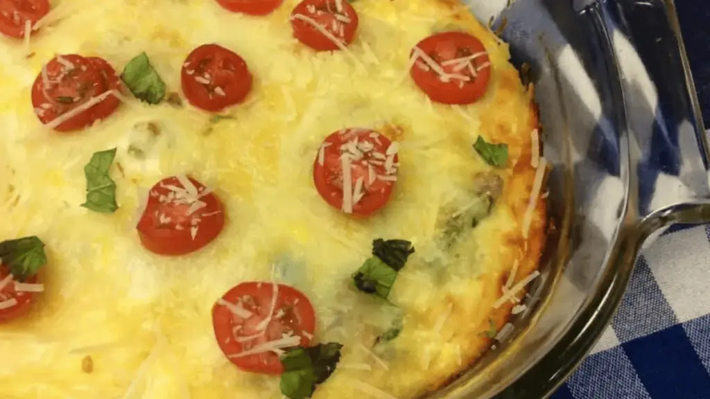 A serving of cheesy spinach egg casserole with tomatoes, on a plate.