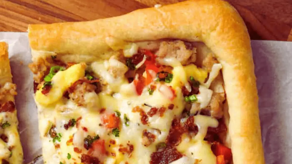 Squares of breakfast pizza with sausage and cheese.