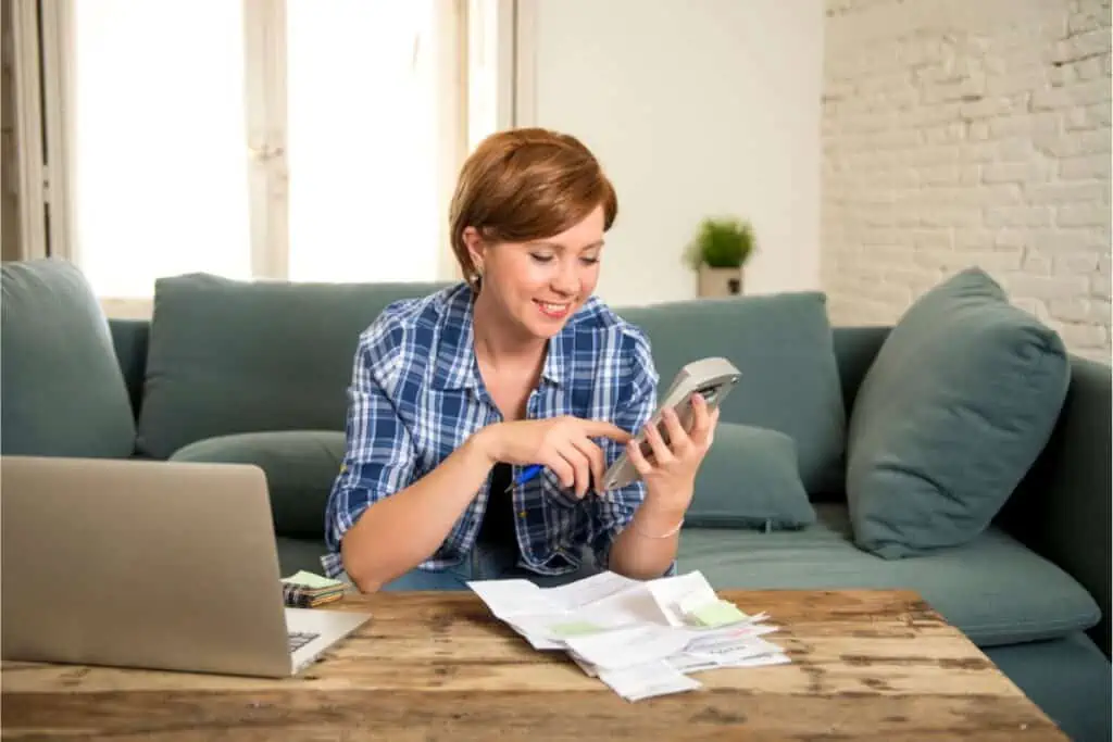 A woman is sitting on a couch, committing household budgeting mistakes while looking at her phone.