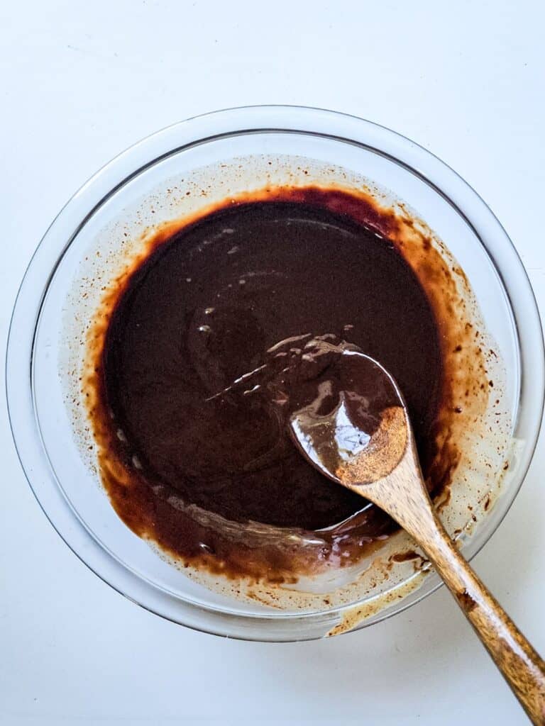 A bowl of mint chocolate chip ice cream cake topped with chocolate sauce, served with a wooden spoon.