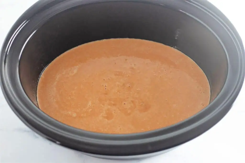 A slow cooker filled with a brown liquid pumpkin cobbler.