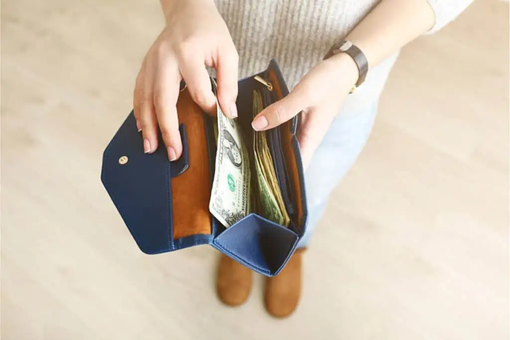A woman saving money on one income holds a blue wallet with cash.