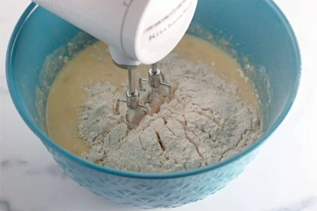 An electric mixer is mixing flour for a Banana Coffee Cake in a bowl.