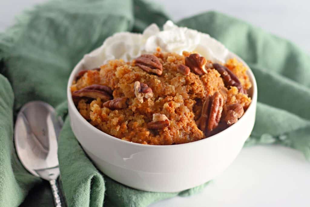 A pumpkin cobbler filled with whipped cream and pecans, served in a white bowl.