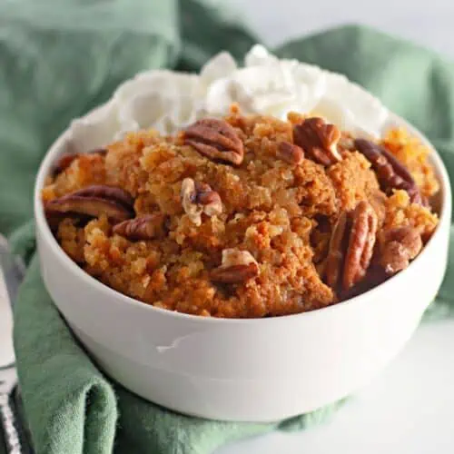 A pumpkin cobbler filled with whipped cream and pecans, served in a white bowl.