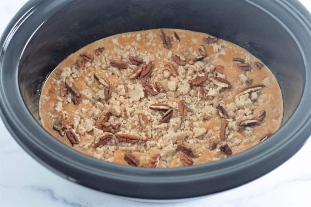 A crock pot filled with pumpkin cobbler and pecans.