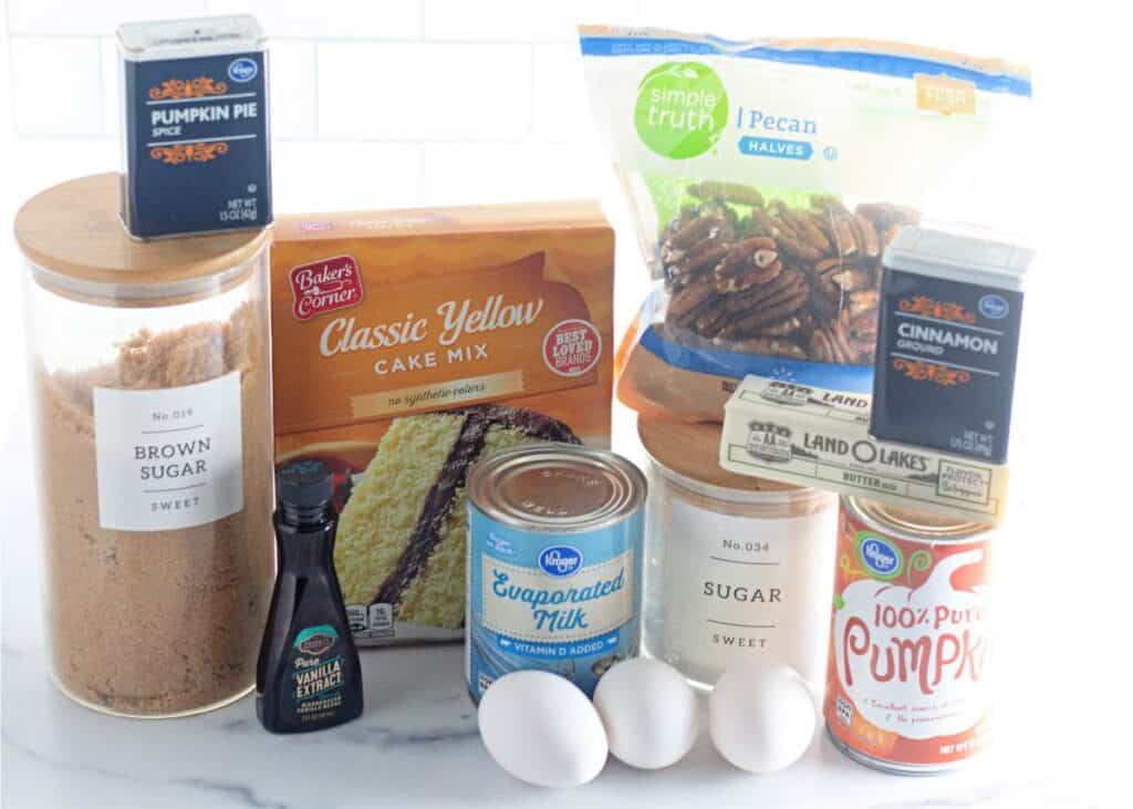 The ingredients for a pumpkin cake, including pumpkin puree and spices, are laid out on a counter.