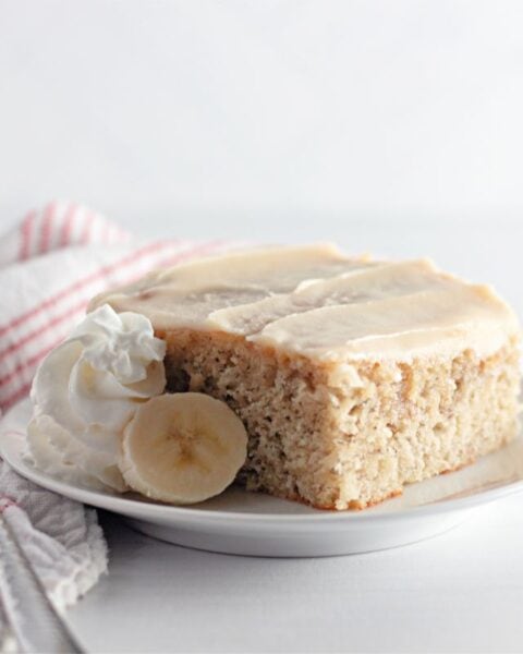 A slice of Banana Coffee Cake adorned with creamy whipped cream and served with a fork.