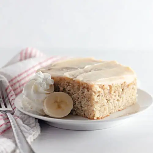 A slice of Banana Coffee Cake adorned with creamy whipped cream and served with a fork.