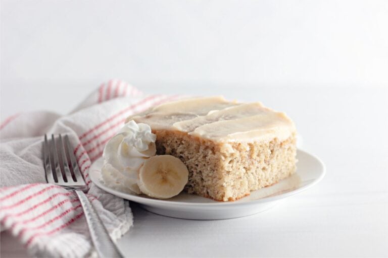 A slice of Banana Coffee Cake adorned with creamy whipped cream and served with a fork.