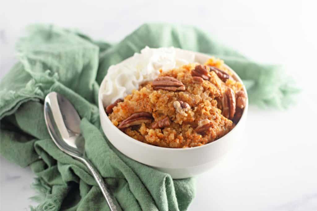 A white bowl with whipped cream, pecans, and pumpkin cobbler.