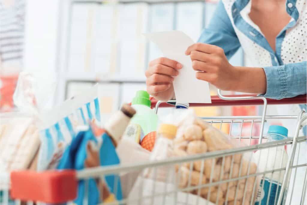 A woman demonstrates how to save on groceries while holding a shopping cart full of items.