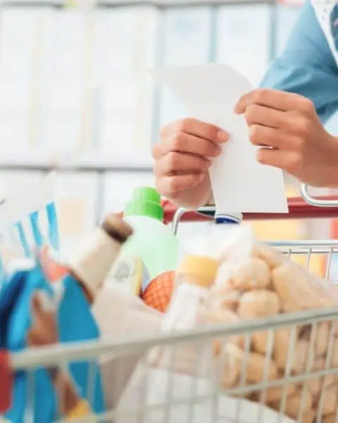 A woman demonstrates how to save on groceries while holding a shopping cart full of items.
