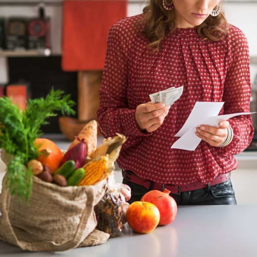 A woman is standing in front of a bag of fruits and vegetables.