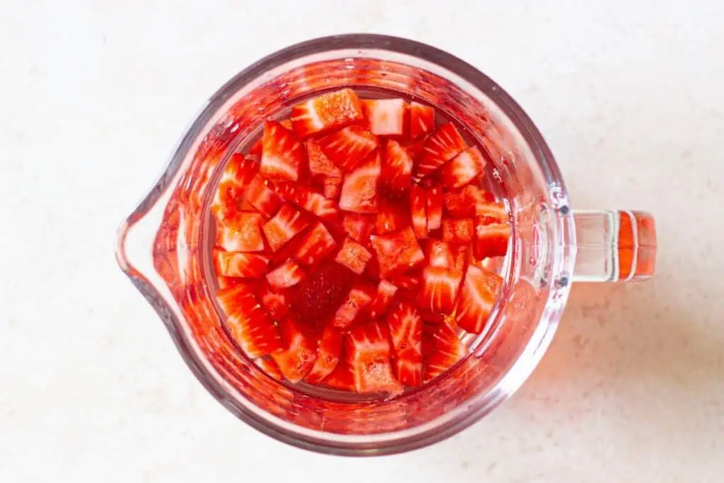 Sliced strawberries blended into Strawberry Acai Refresher on a white surface.