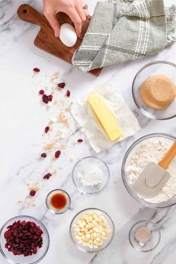 A person follows a recipe, carefully adding cranberry ingredients to a bliss bar mixture on a marble countertop.