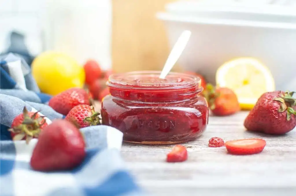 Strawberry jam in a jar with lemons, strawberries and recipe.