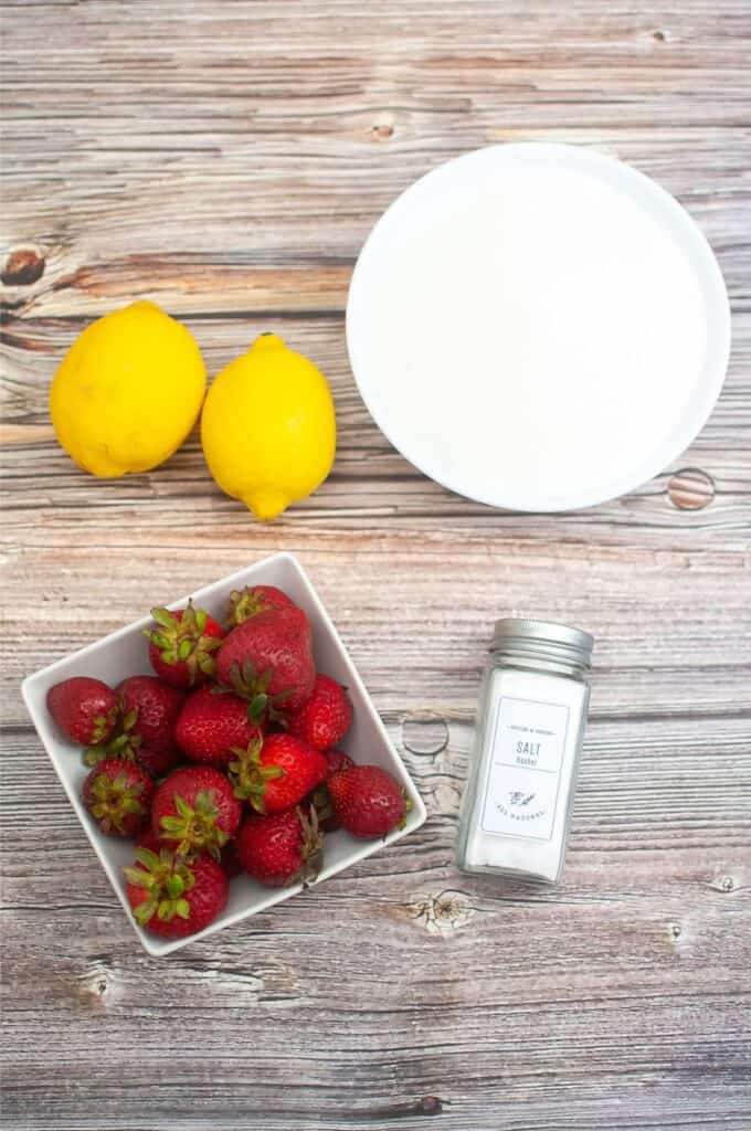 A bowl of strawberries and sugar on a wooden table.