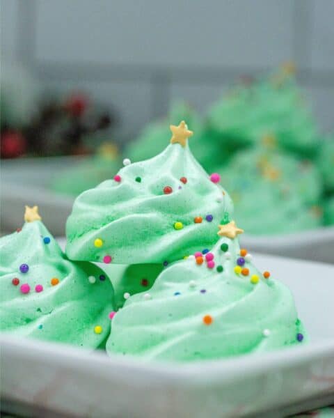 Festive Christmas meringue cookies adorned with colorful sprinkles, delicately arranged on a plate.