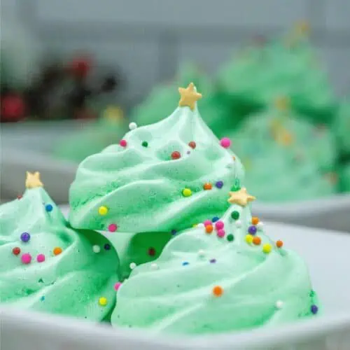 Festive Christmas meringue cookies adorned with colorful sprinkles, delicately arranged on a plate.