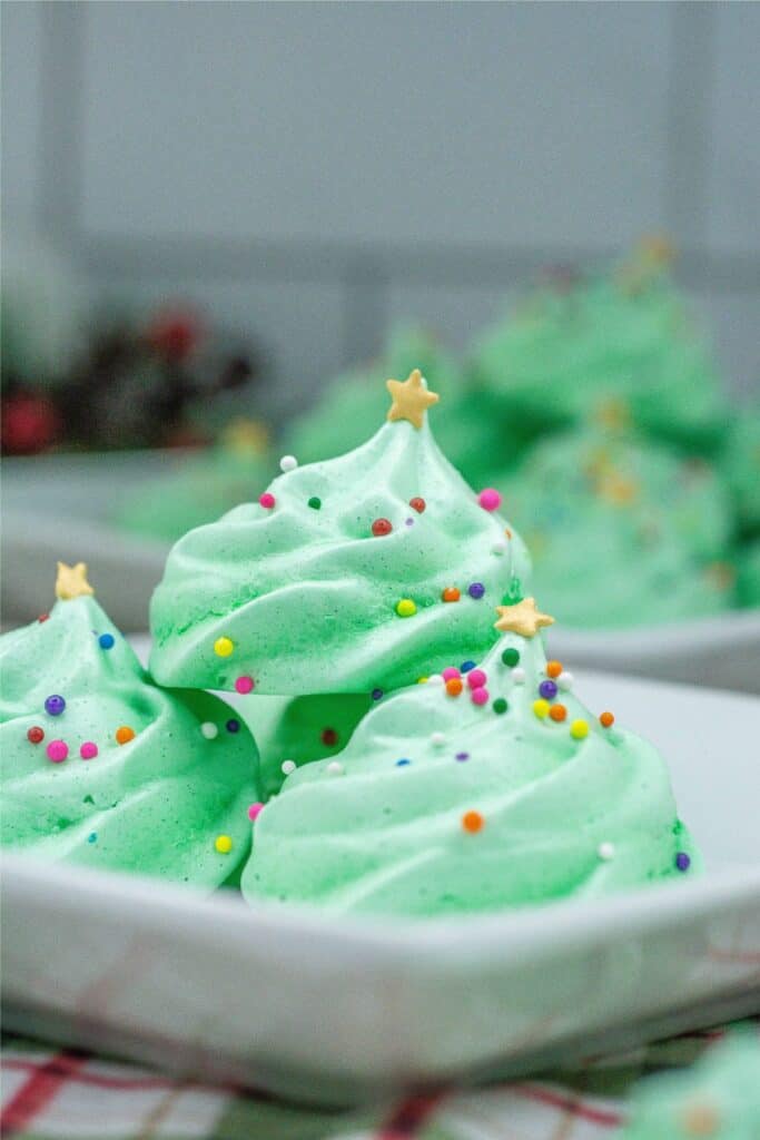Festive Christmas meringue cookies adorned with colorful sprinkles, delicately arranged on a plate.
