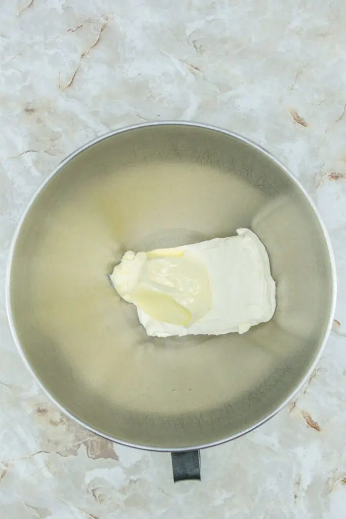 Homemade creamy peppermints placed on a marble surface next to a metal bowl filled with butter.
