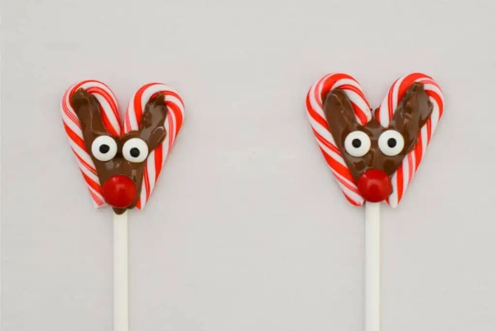 Two reindeer shaped lollipops on a candy cane stick.