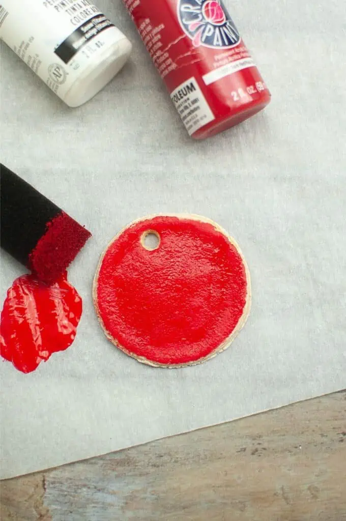 A bottle of red paint and a paint brush creating vibrant ornaments on a piece of paper.