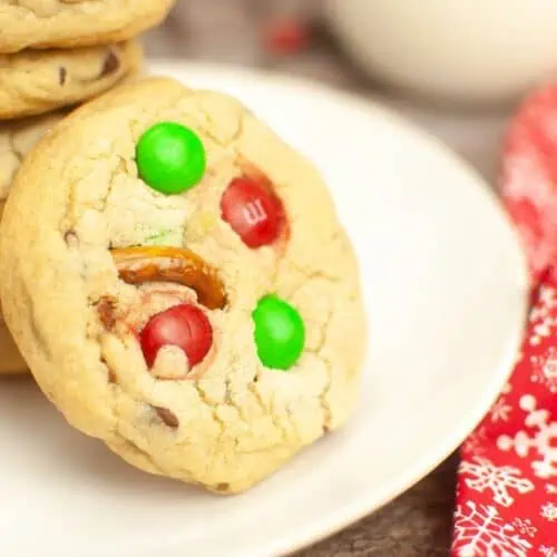 A stack of Christmas cookies with candy canes on a plate, made using the m&m cookie recipe.