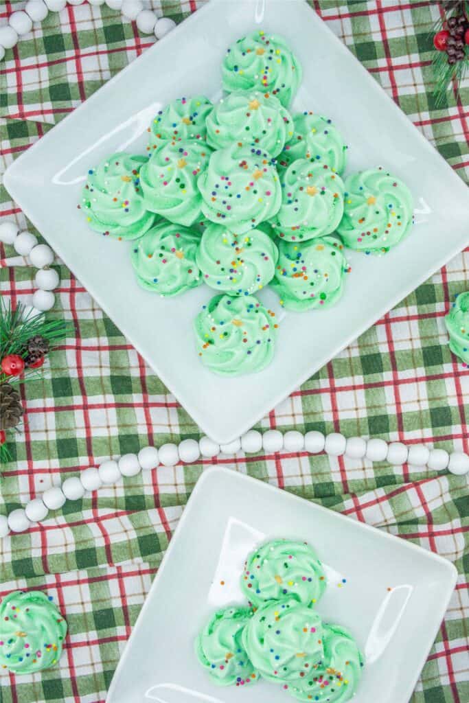 A plate of green frosted cookies decorated like Christmas Trees on a plaid tablecloth.