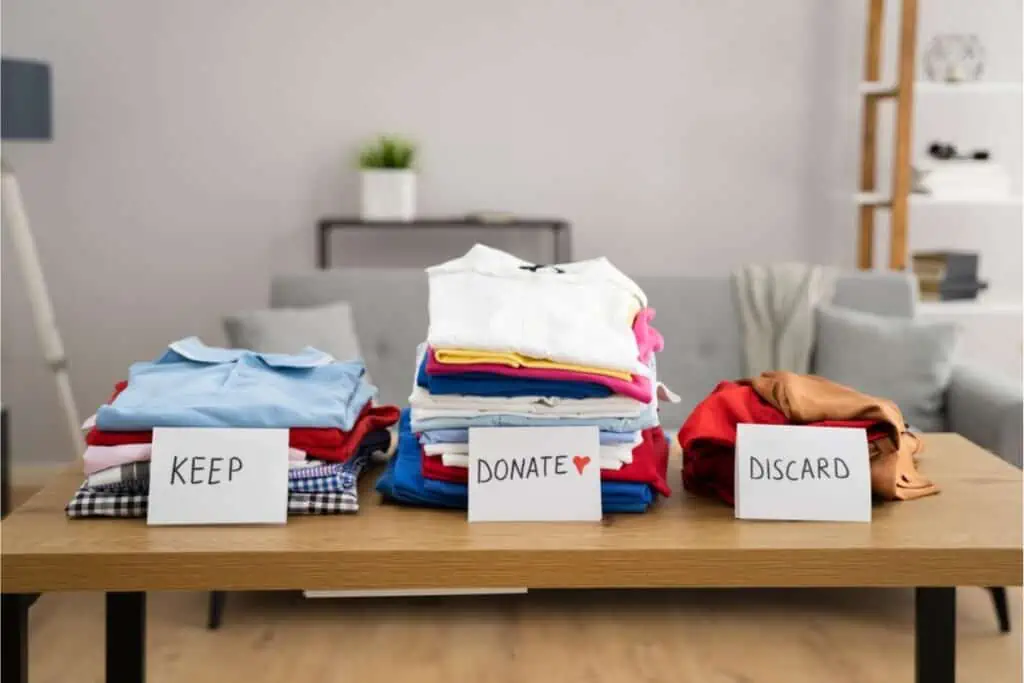 Piles of clothes on a table, waiting to be sorted and decided upon whether to keep or donate. Through this process, individuals can declutter their house and potentially make dreams come true for