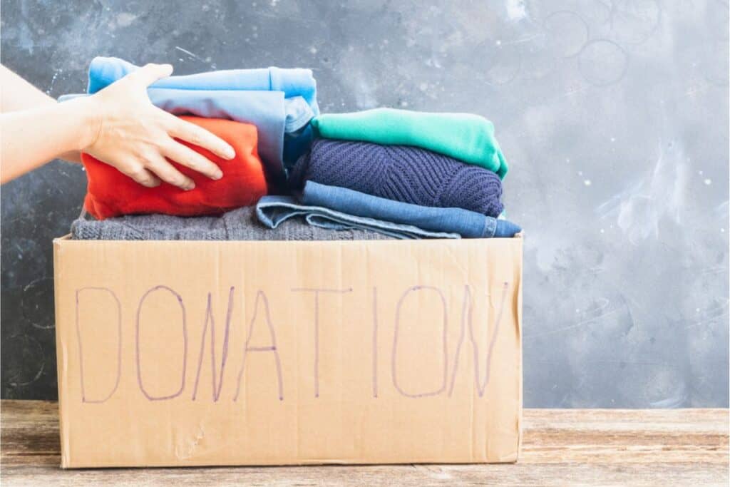 A person is decluttering a house by putting clothes into a cardboard box.