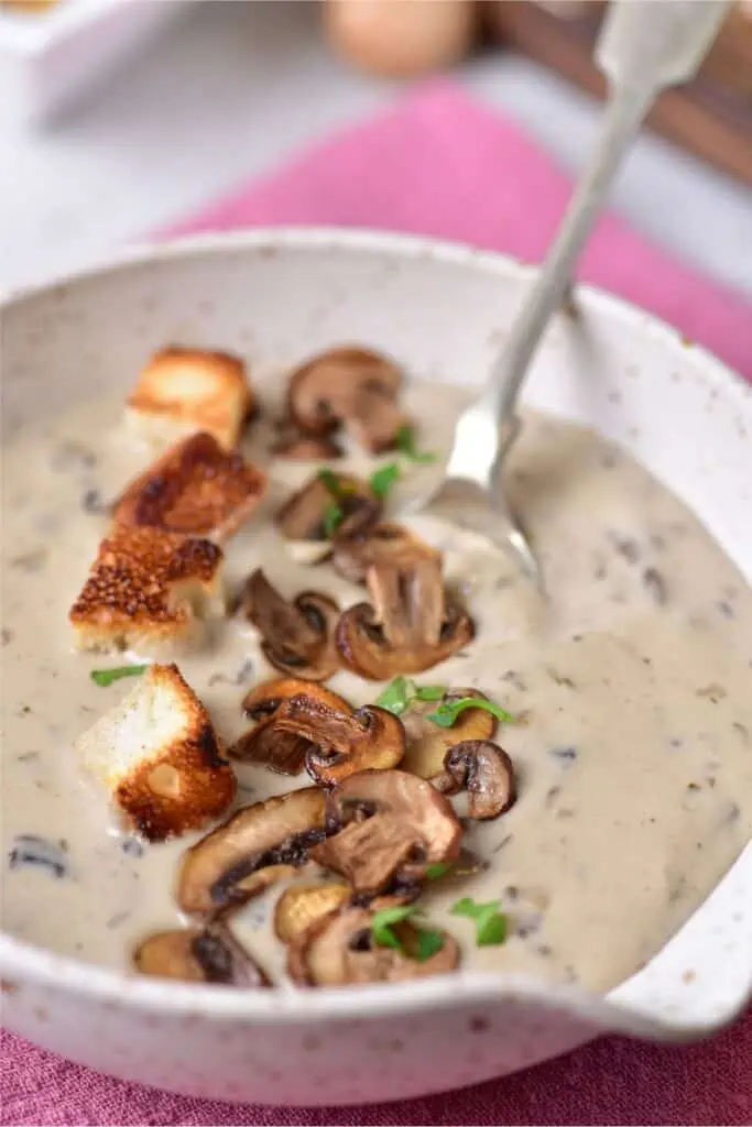 A piping hot bowl of cream of mushroom soup, topped with crispy croutons and ready to be savored with a spoon.
