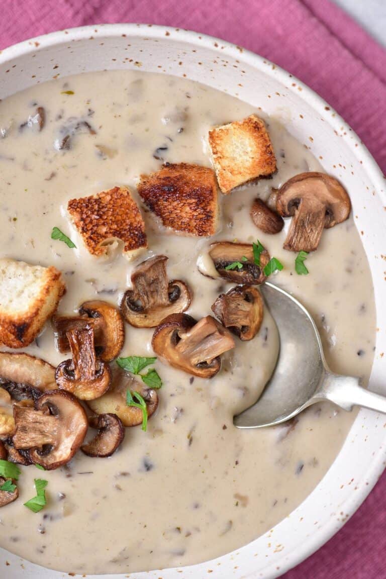 A bowl of cream of mushroom soup with croutons and a spoon.