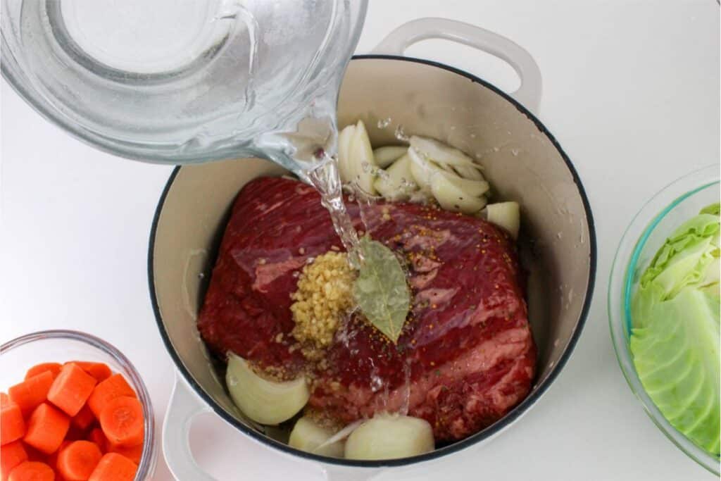 A pot with corned beef, carrots and onions being poured into it.