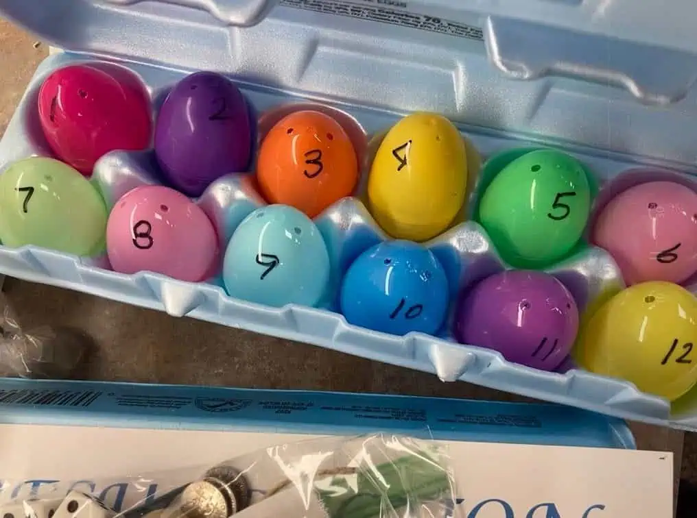 A carton of twelve colorful Resurrection Eggs, numbered 1 to 12 in various shades, with coins and a coupon partially visible nearby.