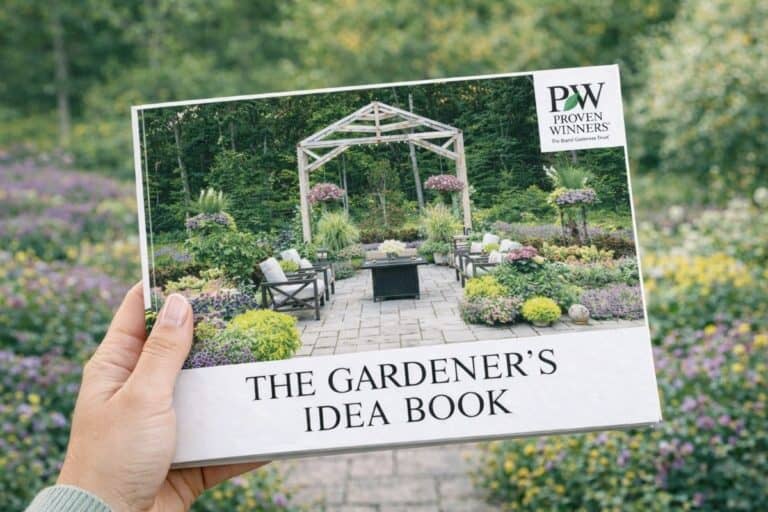 A hand holds a Free Gardener’s Idea Book with a cover image of a landscaped garden featuring a pergola, seating area, and various plants.