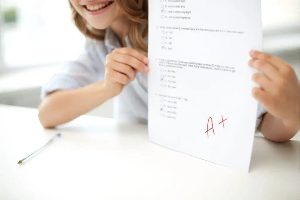 A student proudly holds up a test paper with multiple-choice questions and a red A+ grade, ready to celebrate with Good Report Card Freebies.