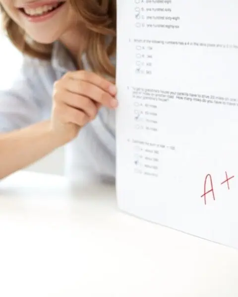 A student proudly holds up a test paper with multiple-choice questions and a red A+ grade, ready to celebrate with Good Report Card Freebies.