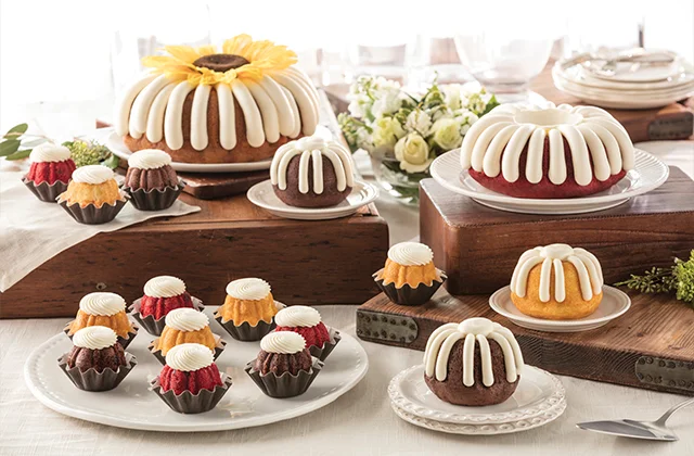 An assortment of bundt cakes and bundtinis with white icing arranged on plates and stands, perfect for celebrating Free Summer Reading Programs at a decorated table.
