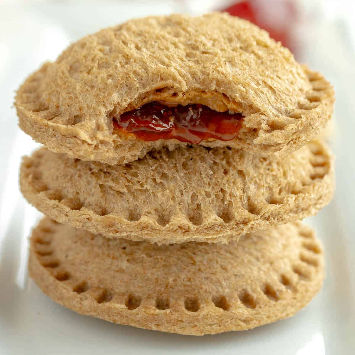 Three round, whole wheat sandwich pockets are stacked, with the top one bitten to reveal a peanut butter and jelly filling—perfect for easy School Lunch Ideas.