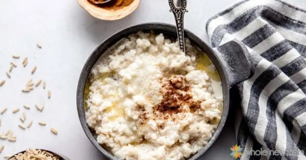 A bowl of creamy oatmeal topped with a sprinkle of cinnamon, next to a silver spoon, a striped cloth, and a small bowl of spices on a white surface—perfect for stress-free mornings.