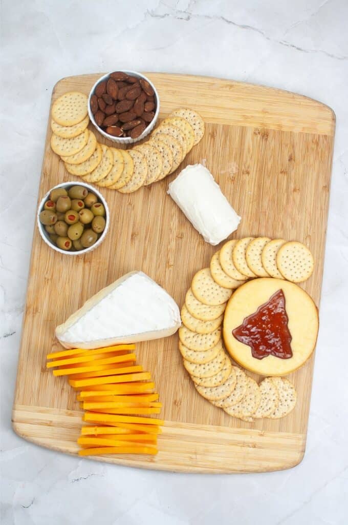 A festive charcuterie board with cheese, crackers, almonds, olives, and jam elegantly arranged on a wooden surface, perfect for Christmas gatherings.
