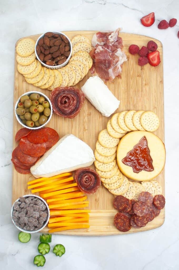 A festive Christmas charcuterie board is elegantly adorned with a selection of cheeses, meats, crackers, olives, almonds, chocolate, and artfully arranged slices of strawberries and raspberries.