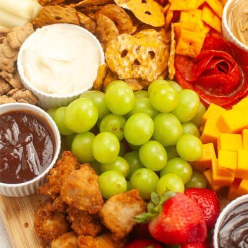 A delightful kids charcuterie board featuring an array of berries, grapes, cheese cubes, crackers, sliced pepperoni, fun fried chicken bites, yummy spreads, and colorful candies. Perfect for little ones to enjoy!.