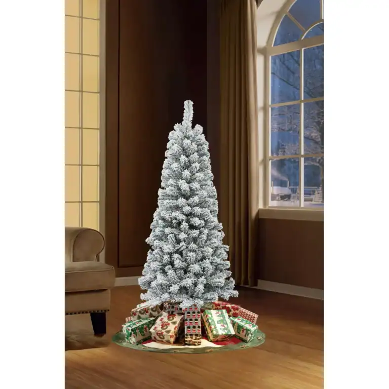 A snow-covered artificial Christmas tree stands festively with colorful wrapped presents underneath, embodying the Christmas spirit. It's perfectly situated in a room with large windows and a brown chair, creating a cozy holiday corner that feels luxurious yet FREE-spirited.
