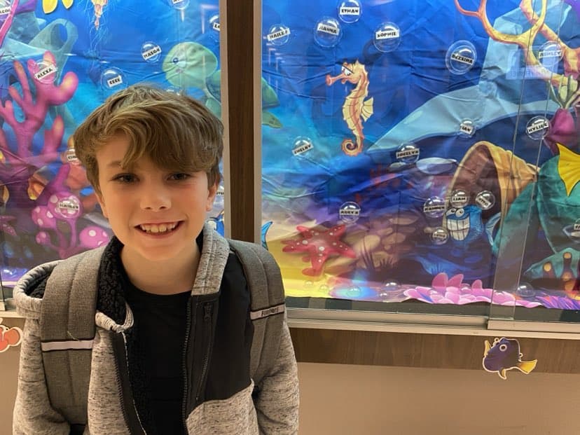 Boy with a backpack smiles in front of a colorful underwater-themed display featuring a seahorse and various sea creatures, reminiscent of some of his favorite things.