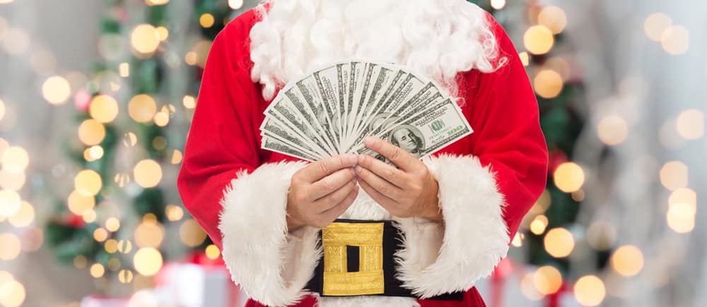 Santa Claus, embodying the essence of stress-free holiday budgeting, proudly displays a fan of hundred-dollar bills against a festive background.